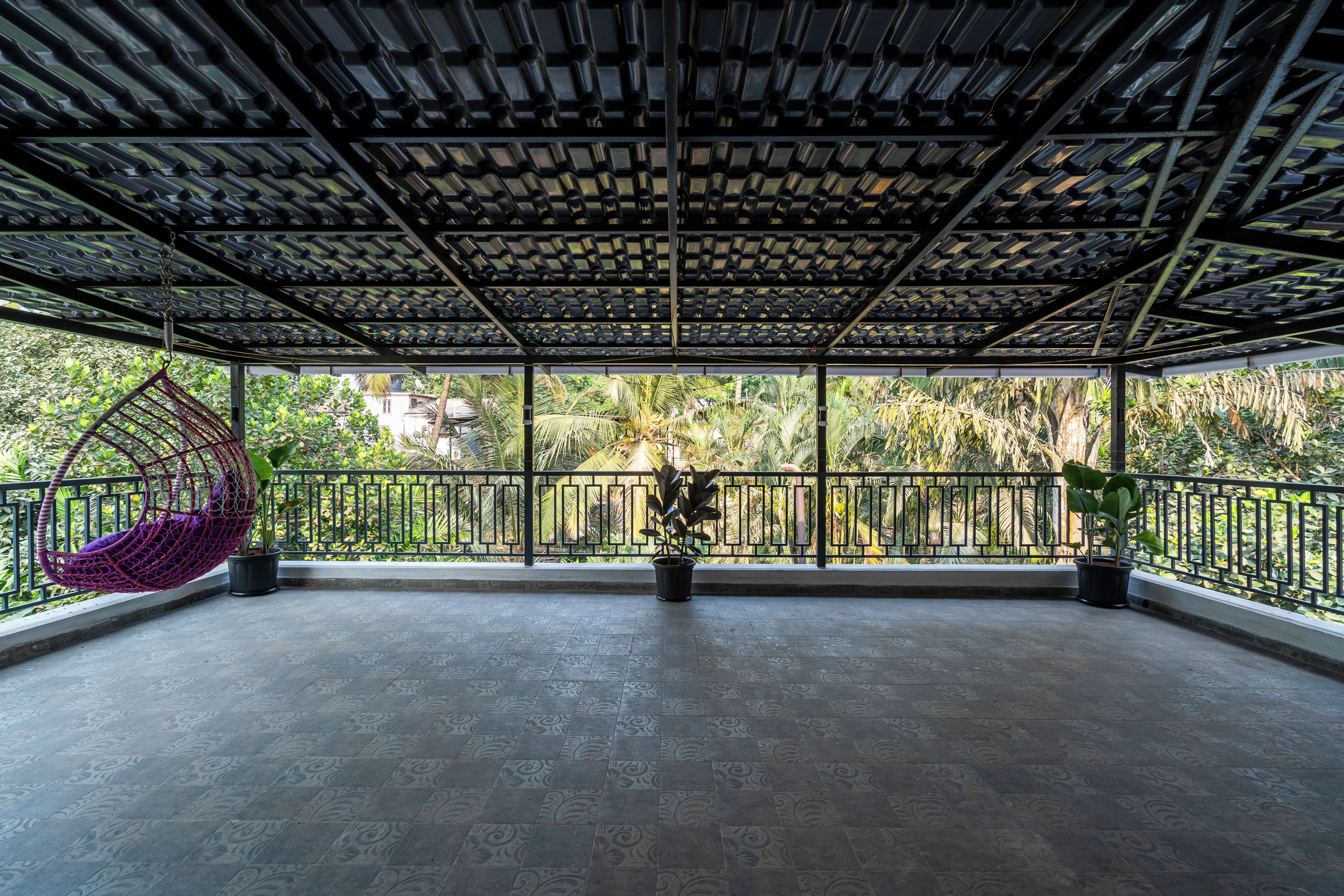 A covered outdoor area with a patterned ceiling, a hanging chair, and potted plants.