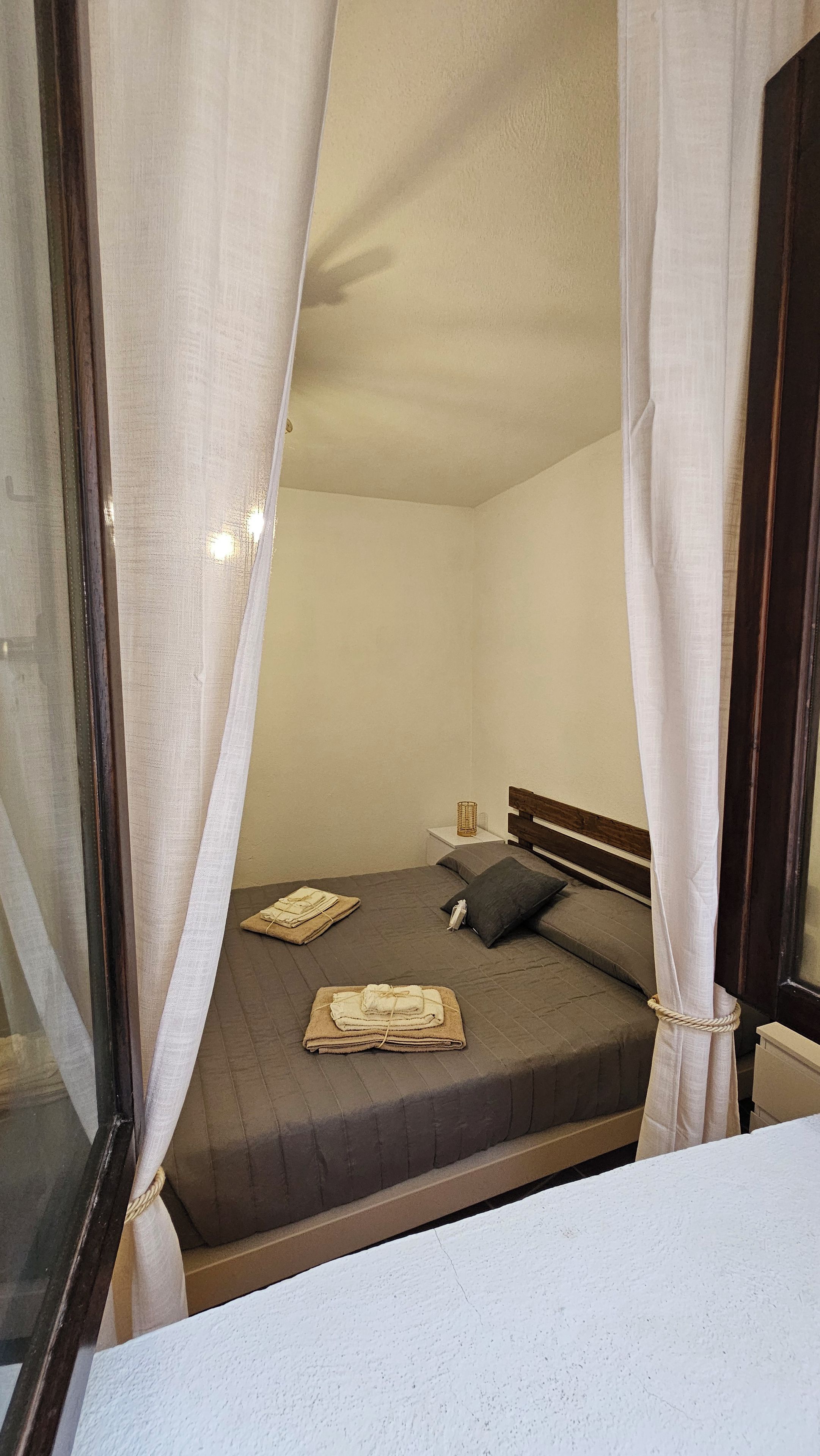 Ein Einzelbett mit Kopfteil, ein Nachttisch mit Lampe und ein Fenster mit Vorhängen.