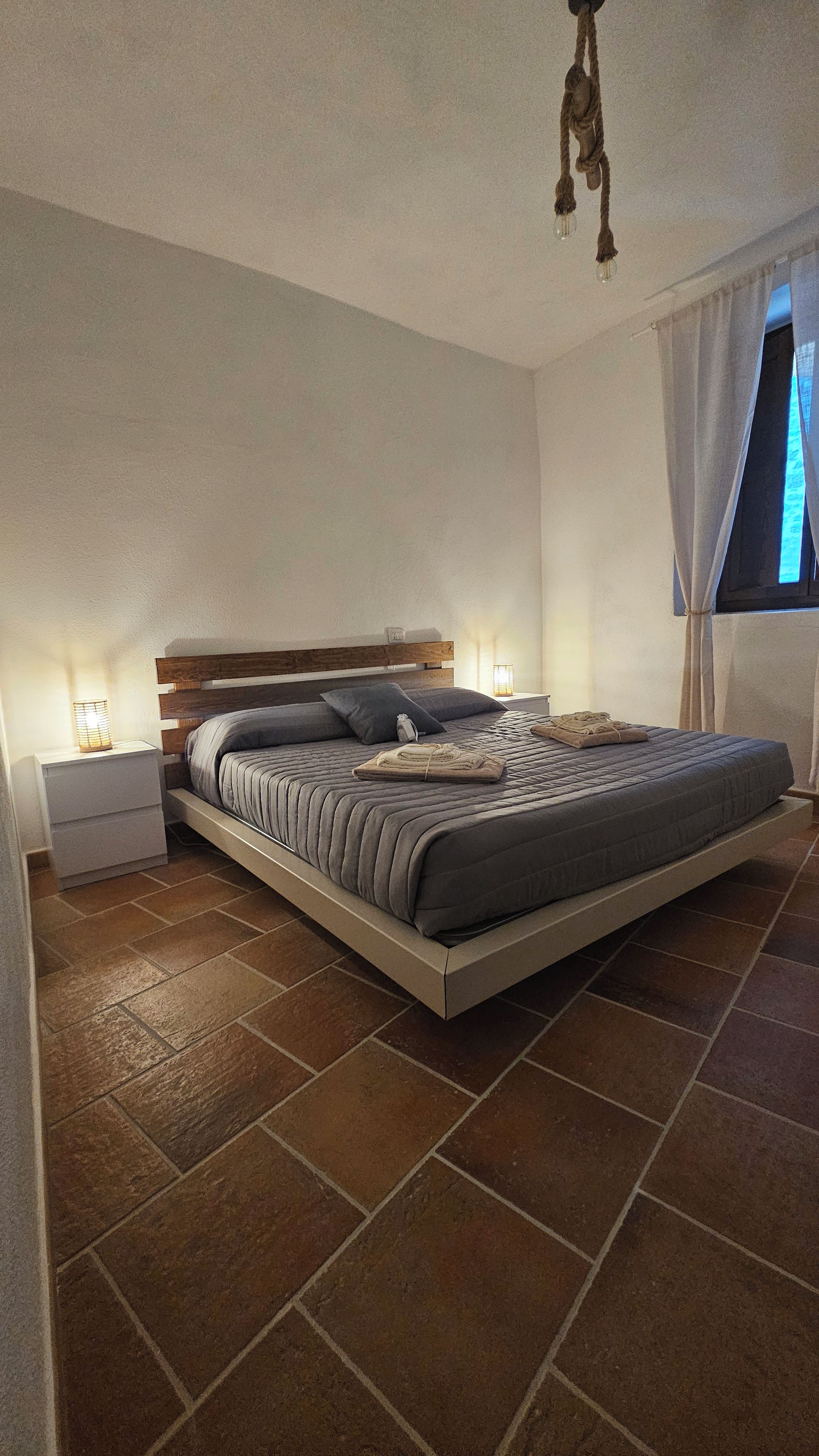 Una camera da letto con un letto, comodini, una lampada e una finestra con tende.