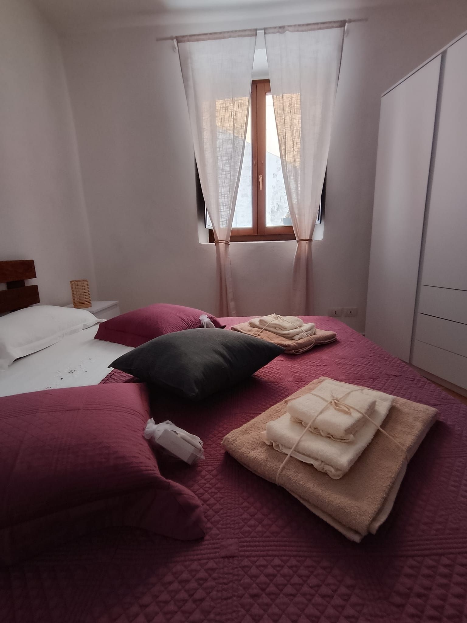 A bedroom with a bed, pillows, a window with curtains, and a wardrobe.