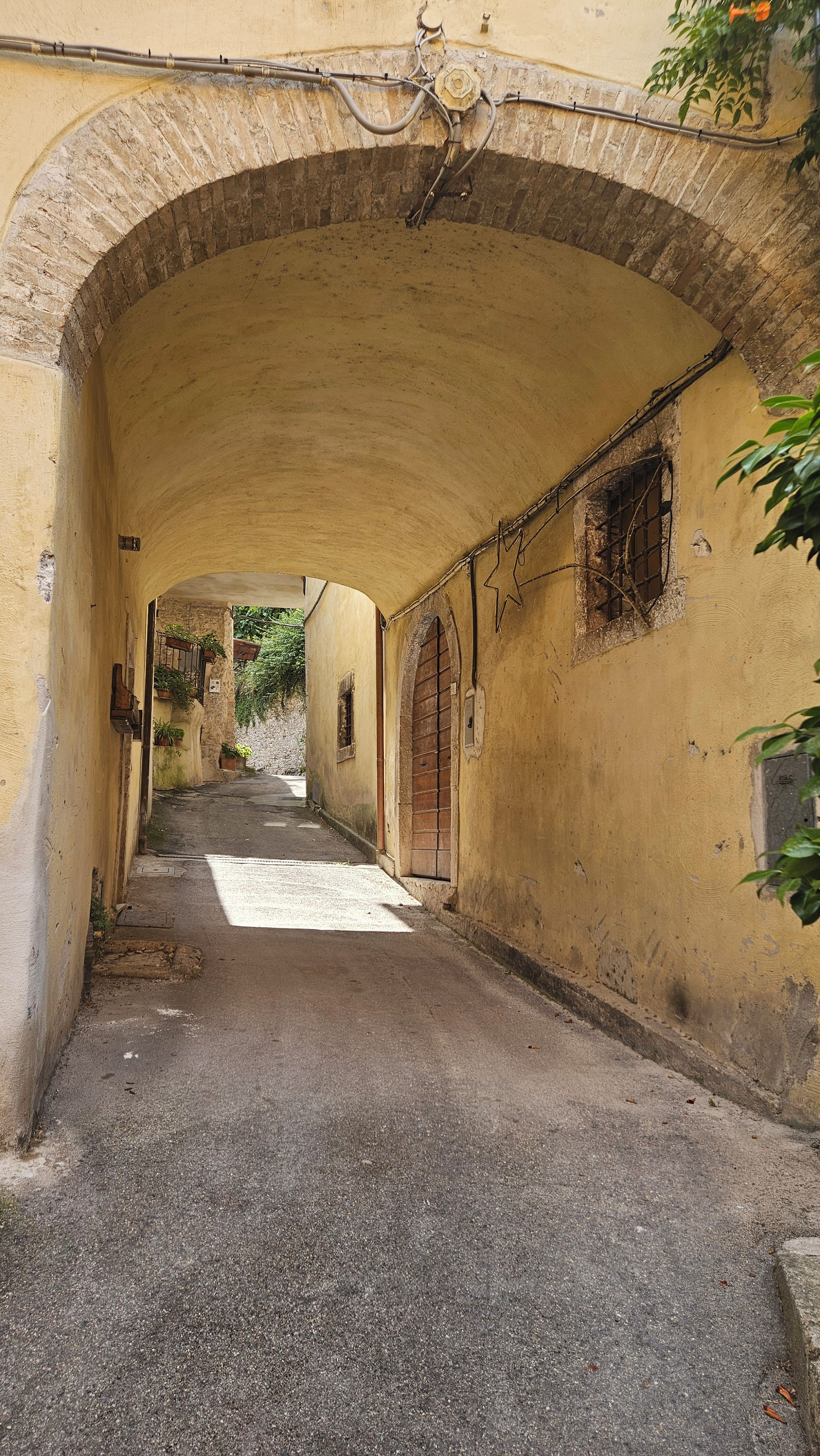 Un estrecho callejón con un arco de piedra, un camino empedrado y un edificio con puerta y ventana de madera.