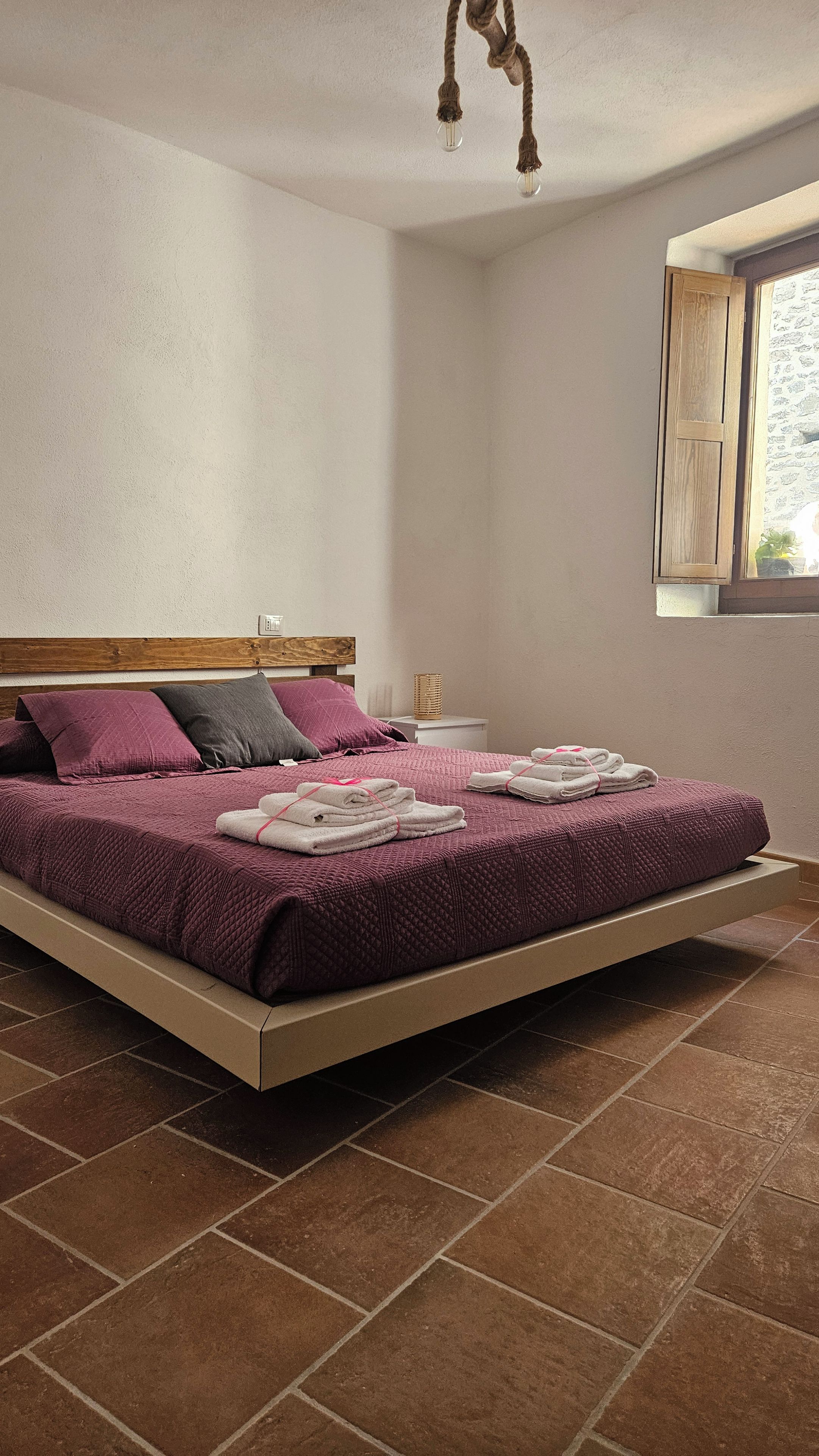 Ein Schlafzimmer mit einem Bett, Kissen, einem Nachttisch, einem Fenster und einer Pendelleuchte.