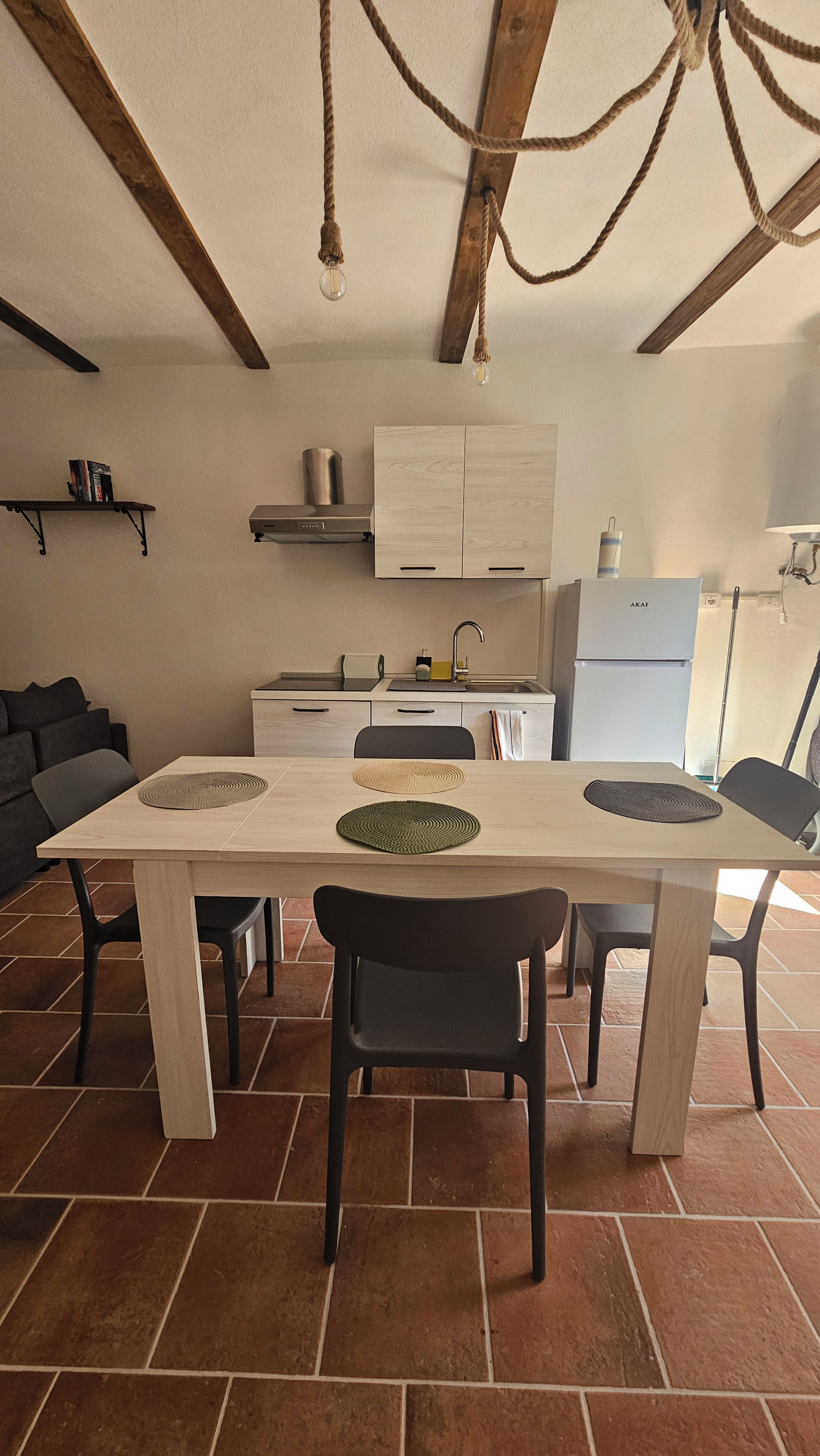A modern kitchen with a central island, a dining table with chairs, and a ceiling with exposed wooden beams and hanging lights.