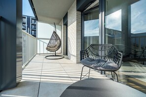 A balcony with a hanging chair, a cushioned bench, and a glass door leading to an outdoor area. - RentPlanet - Apartamenty  Wagonowa (Warszawa)