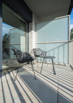 A balcony with two chairs and a table, a glass door, and a view of the sky. - RentPlanet - Apartamenty  Wagonowa (Warszawa)