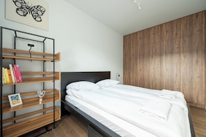 A bedroom with a bed, a wooden wardrobe, a bookshelf, and a wall-mounted light fixture. - RentPlanet - Apartamenty  Wagonowa (Warszawa)