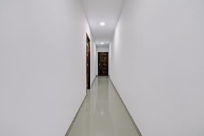 A corridor with white walls and a shiny floor, leading to a door at the end.