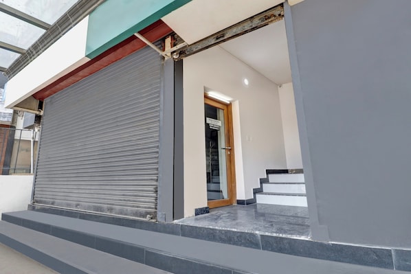 A closed roller shutter door, a set of stairs leading to a wooden door, and a small outdoor area with a metal fence.