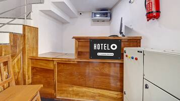 A hotel reception desk with a wooden finish, a fire extinguisher mounted on the wall, and a security intercom system above the desk.