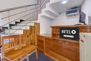 Zona de recepción de un hotel con un escritorio de madera, un letrero que dice 'HOTELO' y una escalera con barandillas de metal.