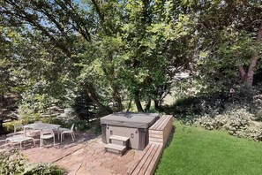An outdoor patio with a hot tub, a table with chairs, and a grassy area. - Balsam House | Baraboo Hot Tub & Bluff Views (Baraboo)