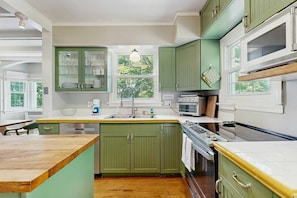 A kitchen with green cabinets, a wooden countertop, a sink, and a window with a view of greenery. - Balsam House | Baraboo Hot Tub & Bluff Views (Baraboo)