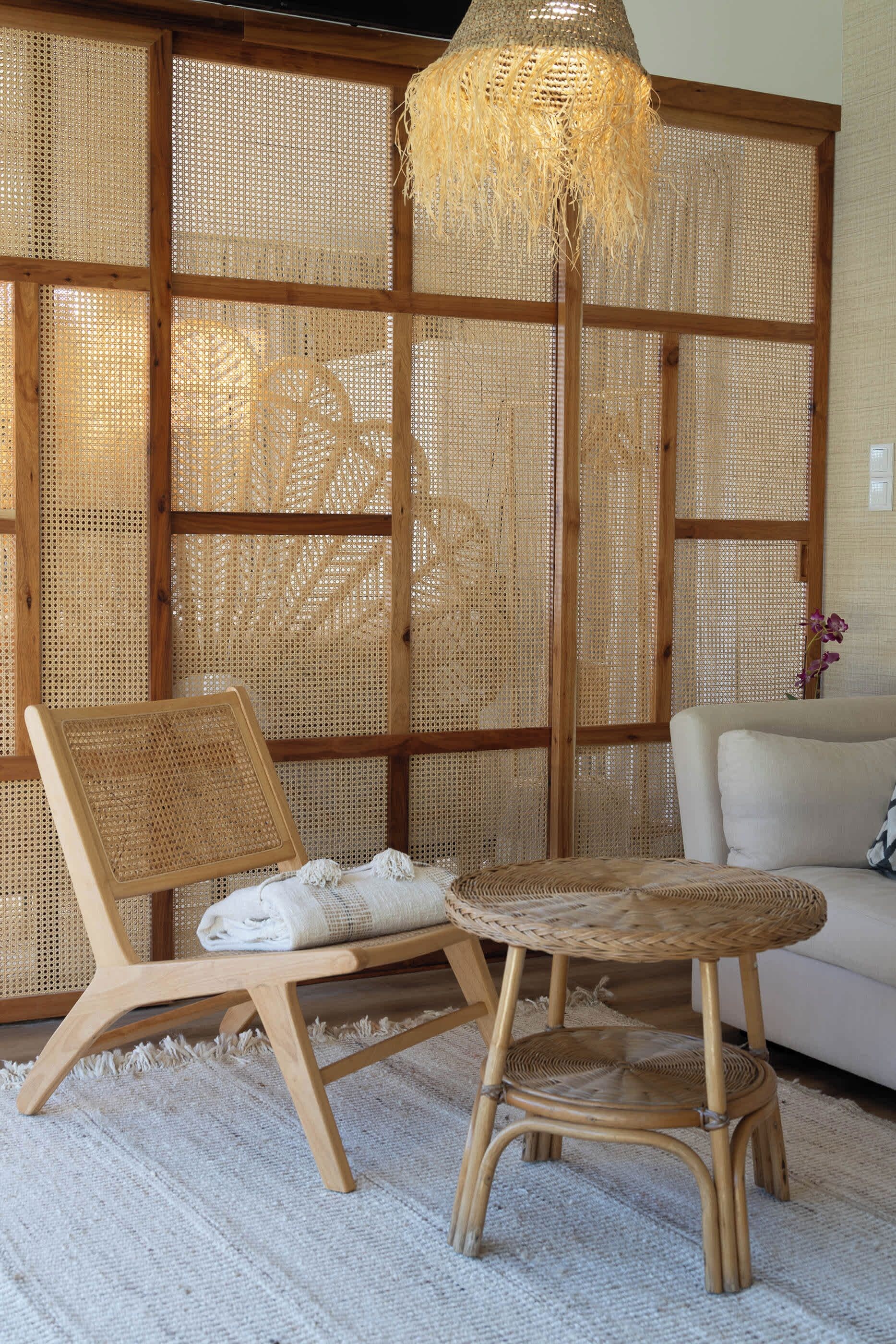 Una habitación con un separador tejido, una silla de ratán, una mesa de ratán y un sofá blanco.