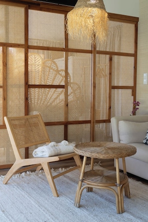 Una habitación con un separador tejido, una silla de ratán, una mesa de ratán y un sofá blanco.