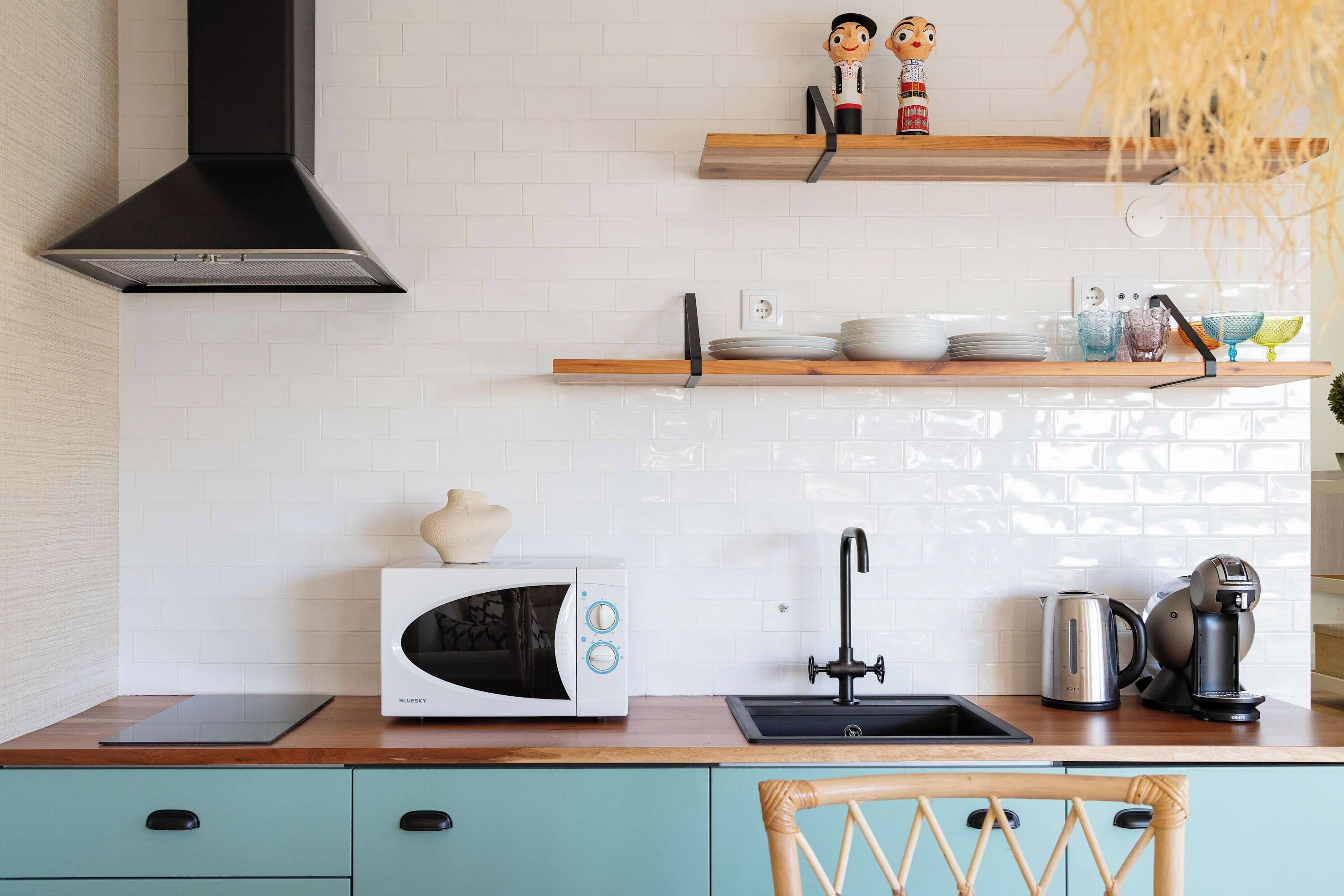 A kitchen with a microwave, kettle, and a sink.