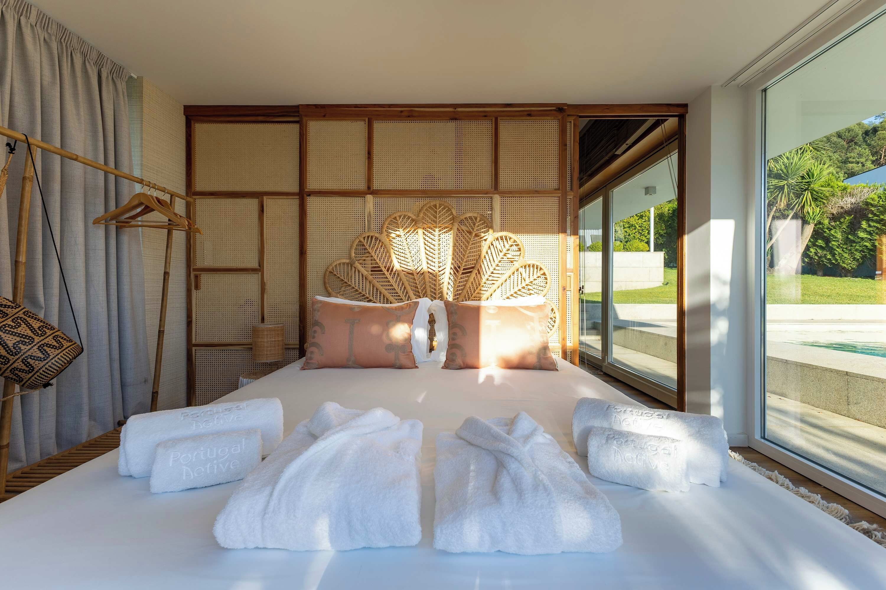 Habitació d'hotel amb un llit gran, una cadira de fusta, una làmpada penjant i vista a una piscina.