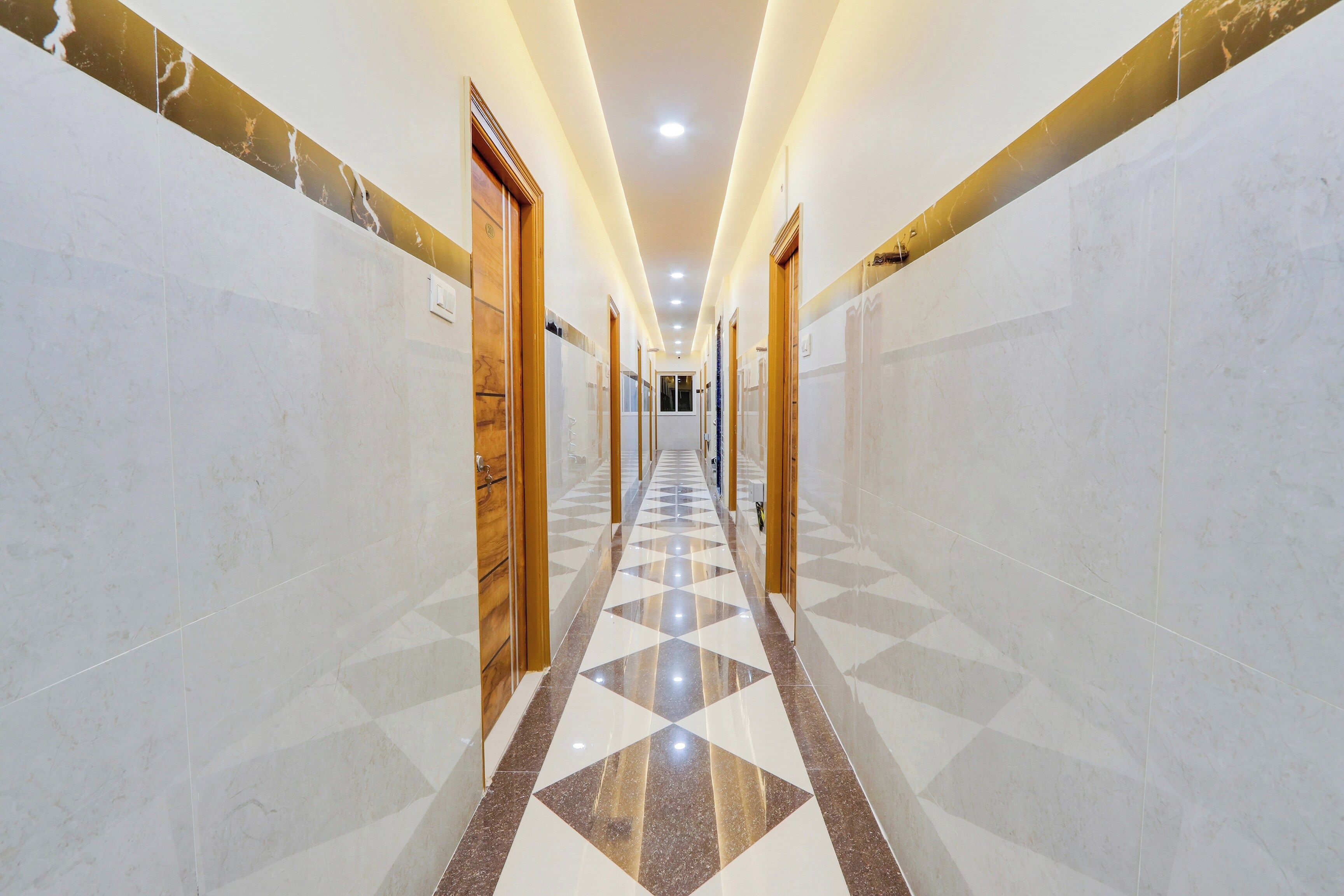 Un largo y estrecho pasillo con piso a cuadros, flanqueado por paredes de mármol y puertas de madera.