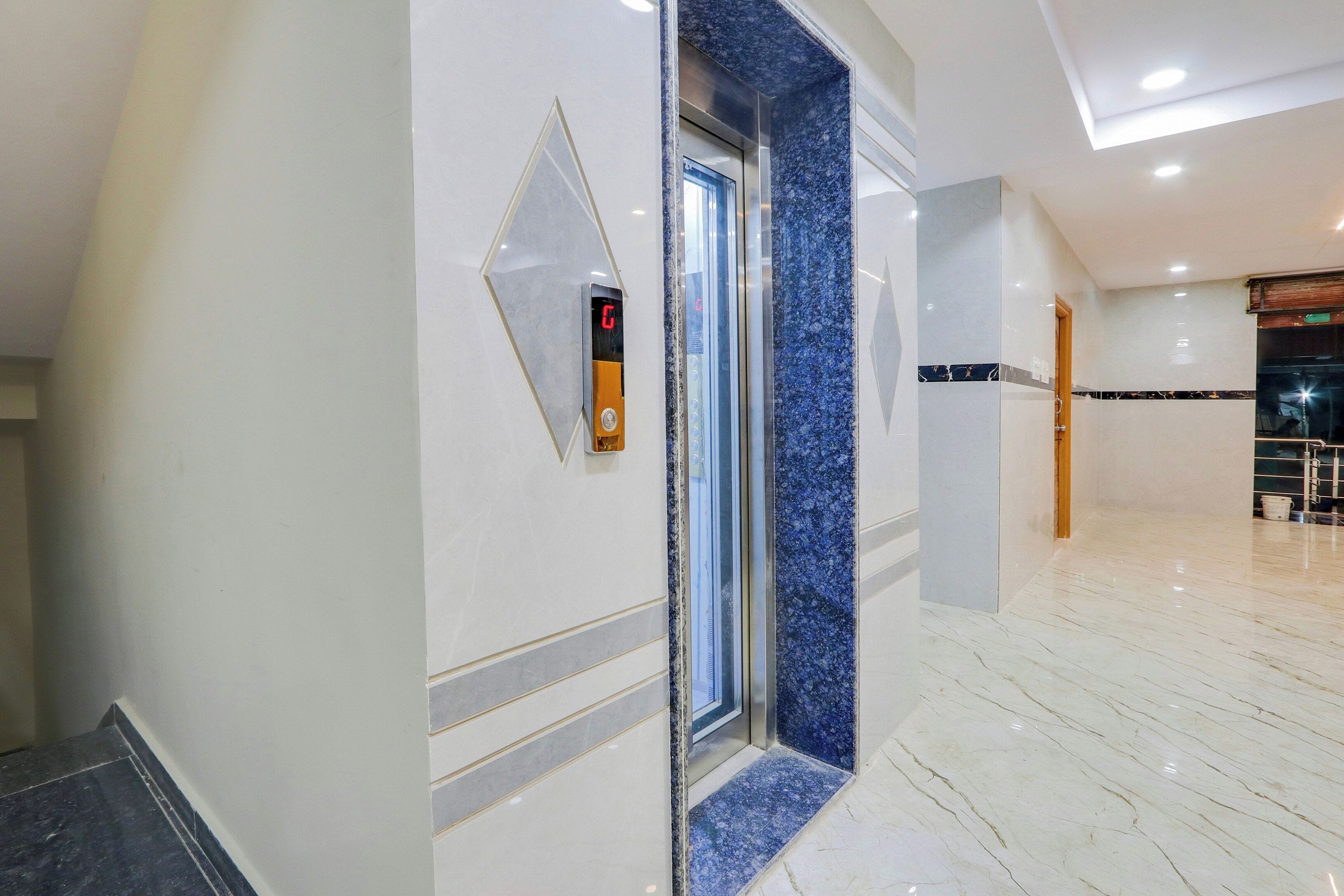 Un ascensor moderno con pantalla digital, piso de mármol y un pasillo con puerta de madera.