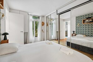 Une chambre moderne avec un grand lit, une armoire et une salle de bain visible à travers une porte ouverte.