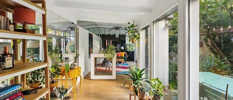 Un interior moderno con suelo de madera, una zona de estar central con un sofá y sillones, y una estantería llena de libros y objetos decorativos.