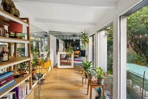 A modern interior with a wooden floor, a central seating area with a sofa and chairs, and a bookshelf filled with books and decorative items. - Pilon | Ground-Floor Apartment with Private Garden in Montmartre (Paris)