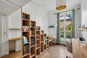 Une pièce avec une bibliothèque en bois remplie de livres, une fenêtre avec des rideaux et un radiateur.
