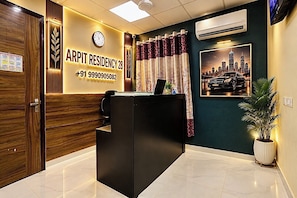 A reception desk with a clock, a cityscape poster, and a contact number. - Arpit Residency 28 (Gurugram)
