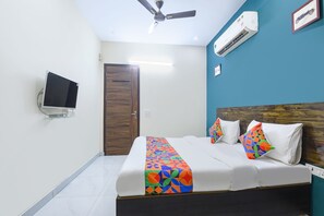 Un dormitorio con cama, ventilador de techo, unidad de aire acondicionado, televisor y una puerta.