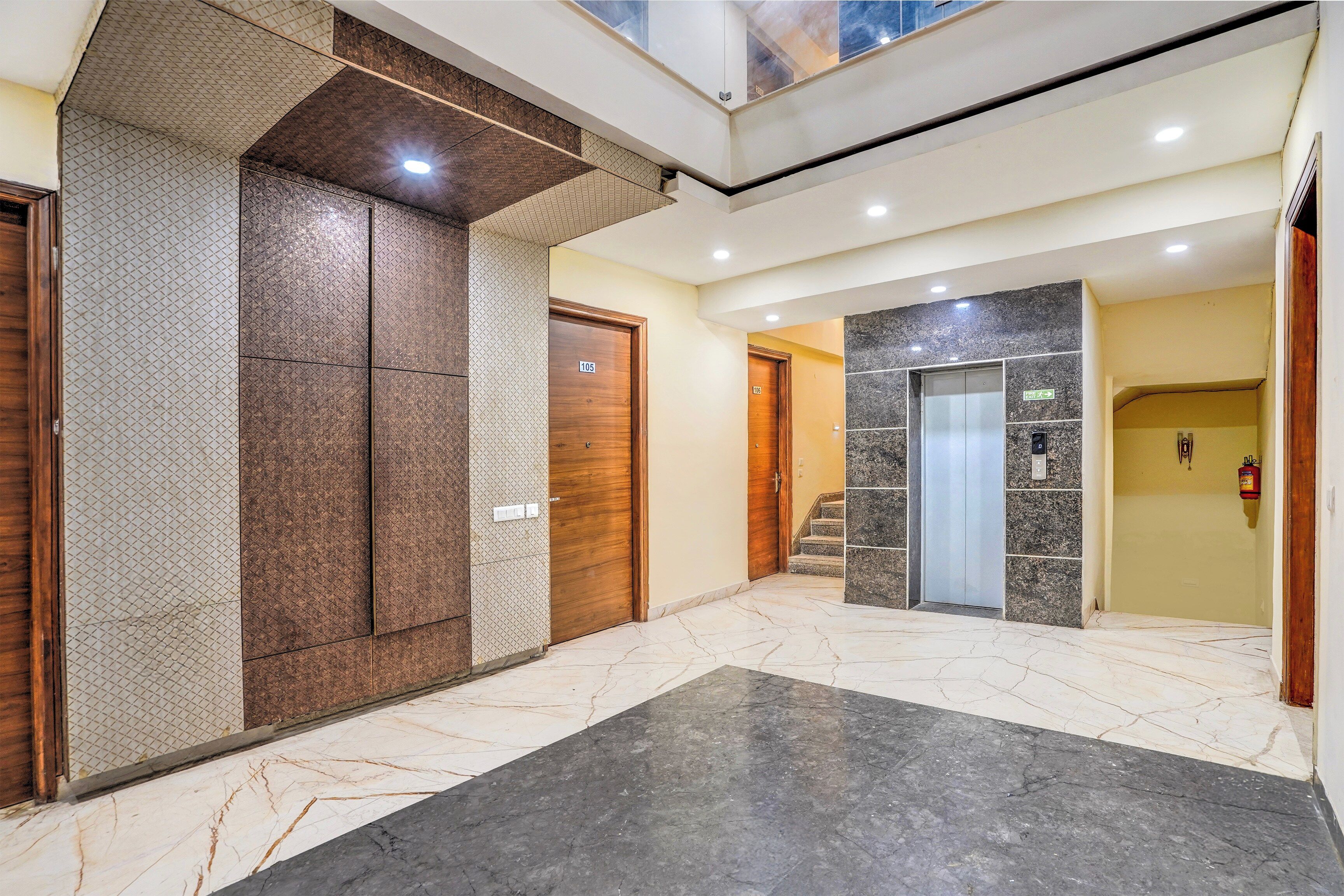 A hotel lobby with a marble floor, a wooden door, and an elevator.