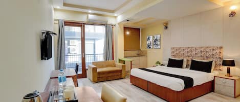 Habitación de hotel con cama, escritorio, silla, mesita con tetera y tazas, y vista al exterior.