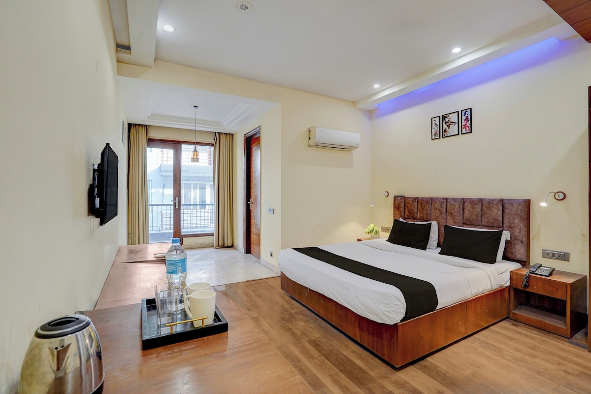 A hotel room with a bed, bedside table, lamp, and a view of the outside.