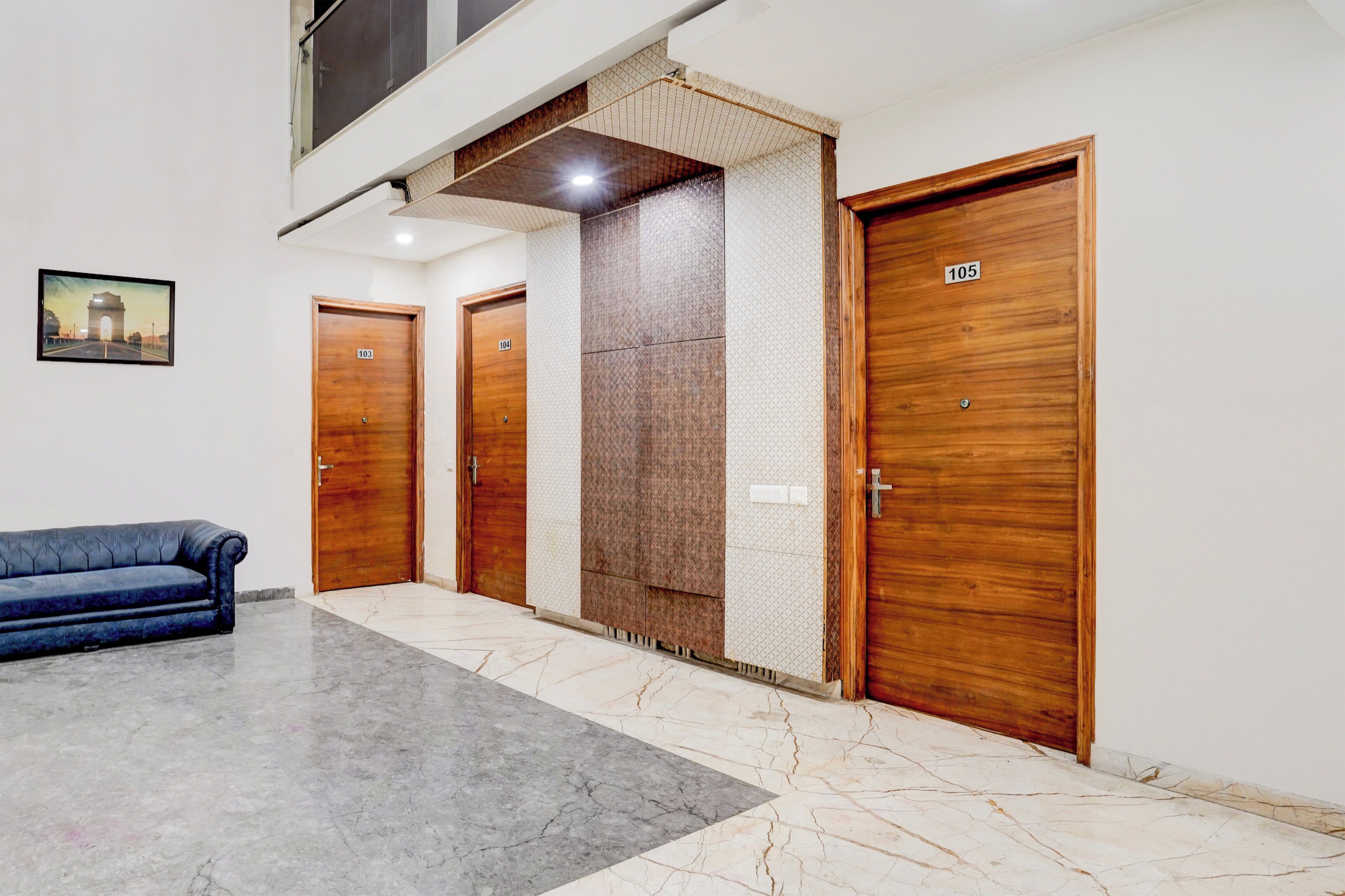 A hotel lobby with three wooden doors, a blue sofa, and a framed picture on the wall.