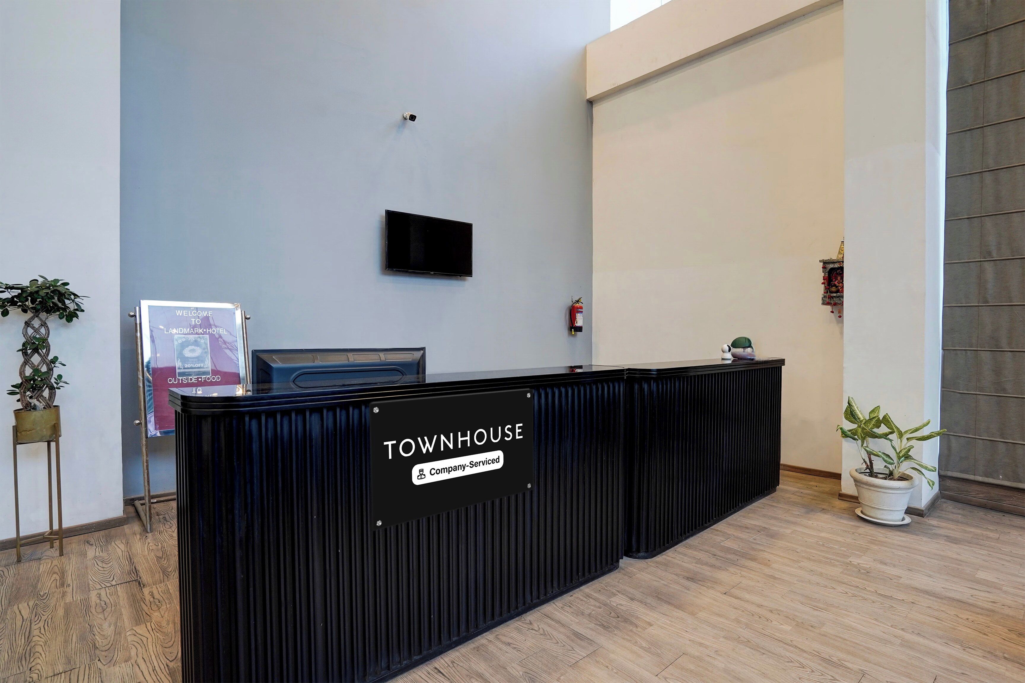A reception desk labeled 'TOWNHOUSE' with a flat-screen TV above it, a fire extinguisher on the wall, and a signboard for 'OUTSIDE FOOD' to the left.