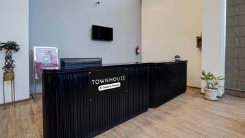 A reception desk labeled 'TOWNHOUSE' with a flat-screen TV above it, a fire extinguisher on the wall, and a signboard for 'OUTSIDE FOOD' to the left.