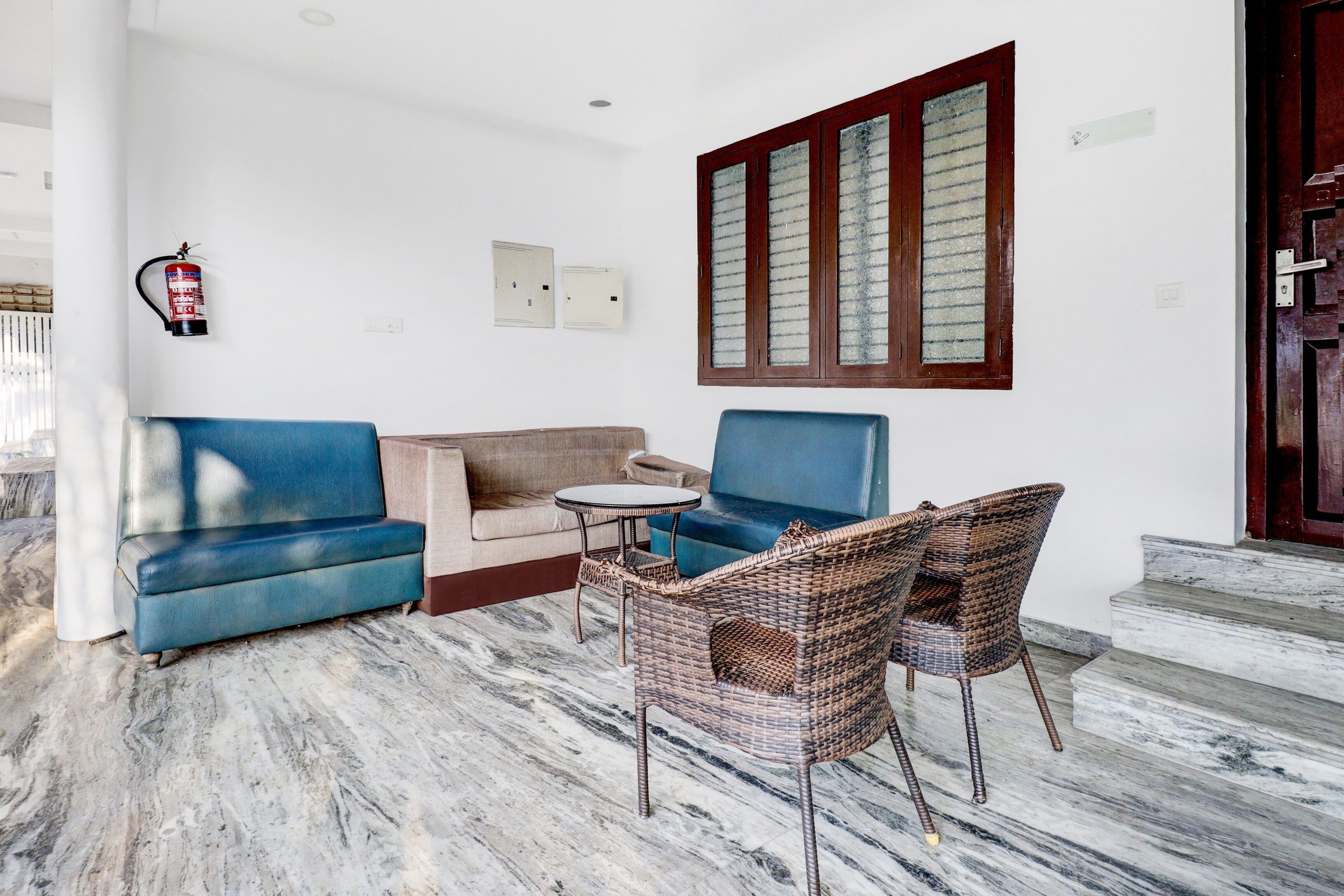 A living area with a sofa, two chairs, a small table, and a fire extinguisher on the wall.