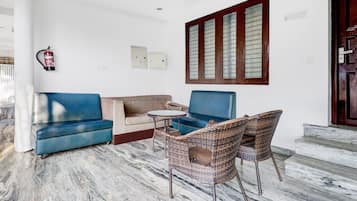 A living area with a sofa, two chairs, a small table, and a fire extinguisher on the wall.