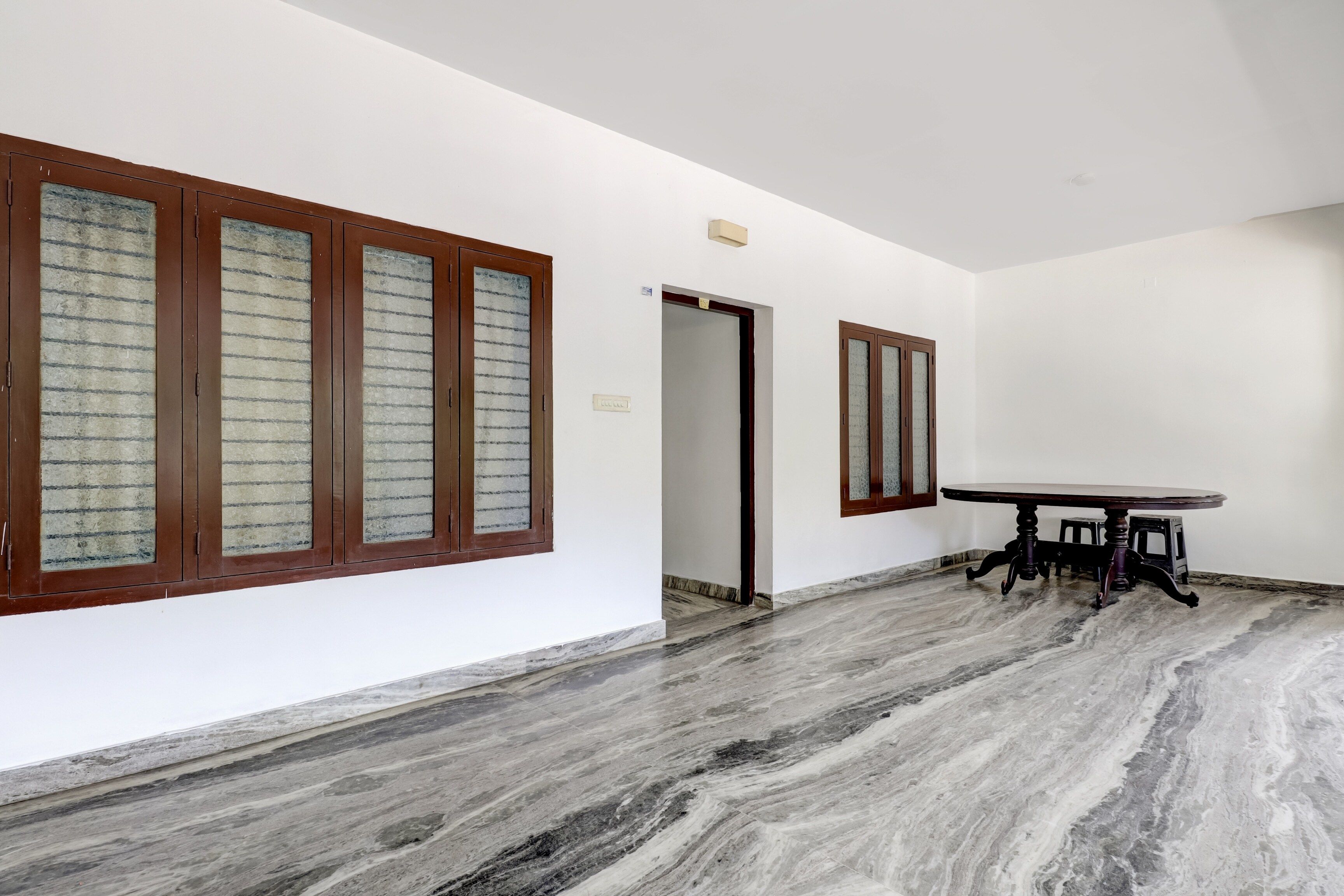Quarto amplo com piso de mármore, uma mesa redonda com cadeiras e grandes janelas com molduras de madeira.