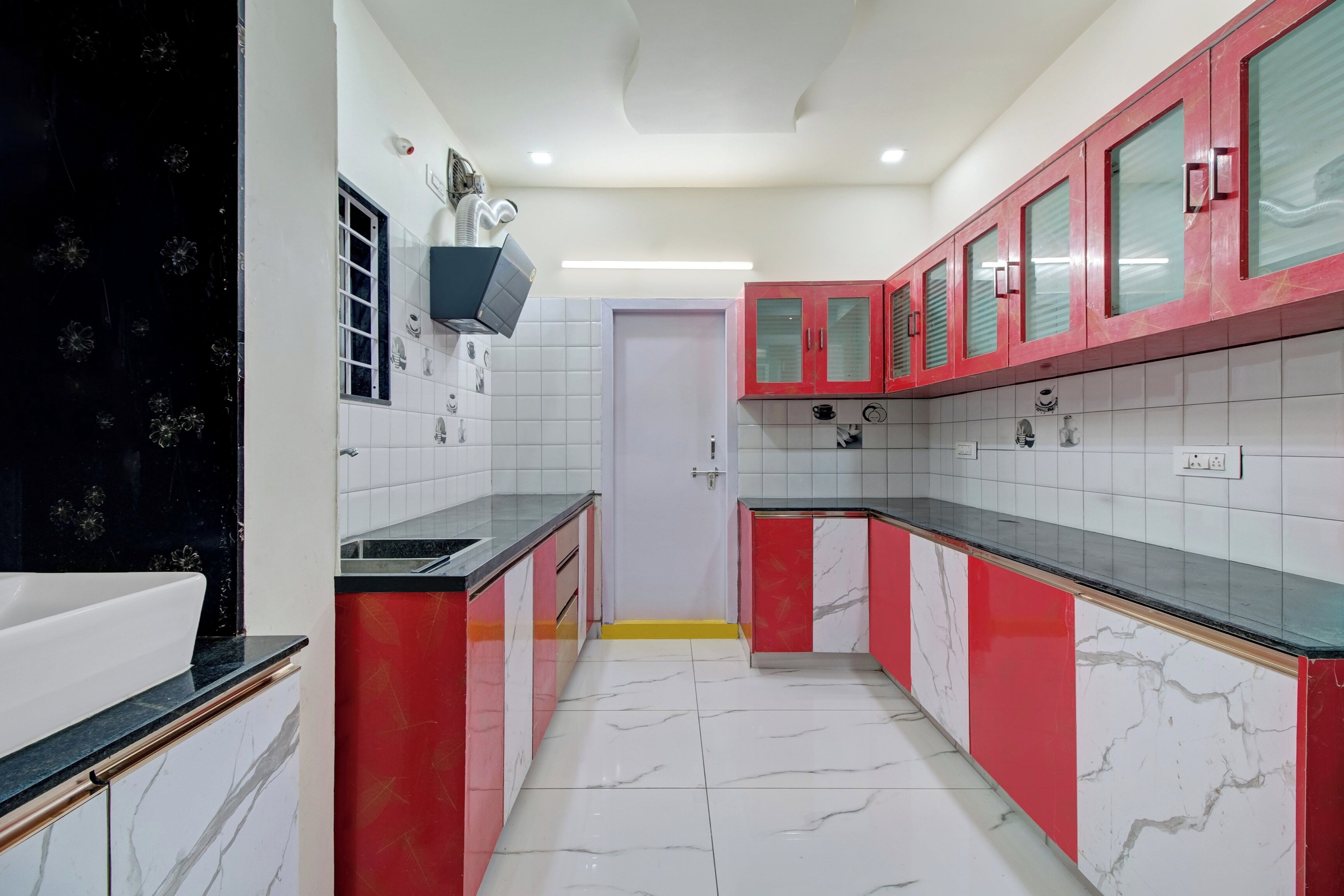 Une cuisine avec des meubles de couleur rouge, des carreaux blancs et un plan de travail noir.