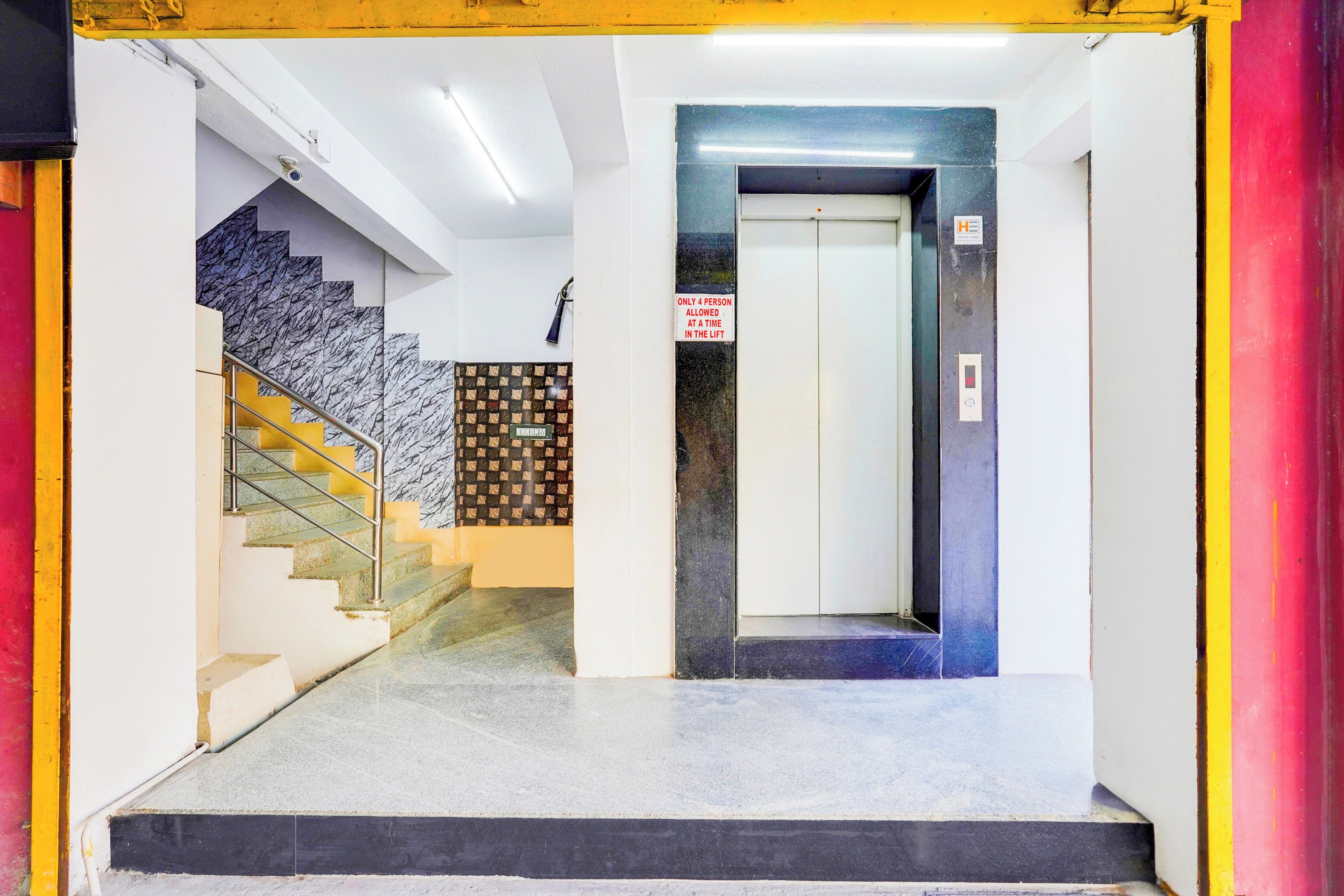 Un vestíbulo de hotel con una escalera de mármol, un ascensor y un letrero que indica un máximo de cuatro personas por viaje en el ascensor.