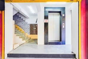 Un vestíbulo de hotel con una escalera de mármol, un ascensor y un letrero que indica un máximo de cuatro personas por viaje en el ascensor.