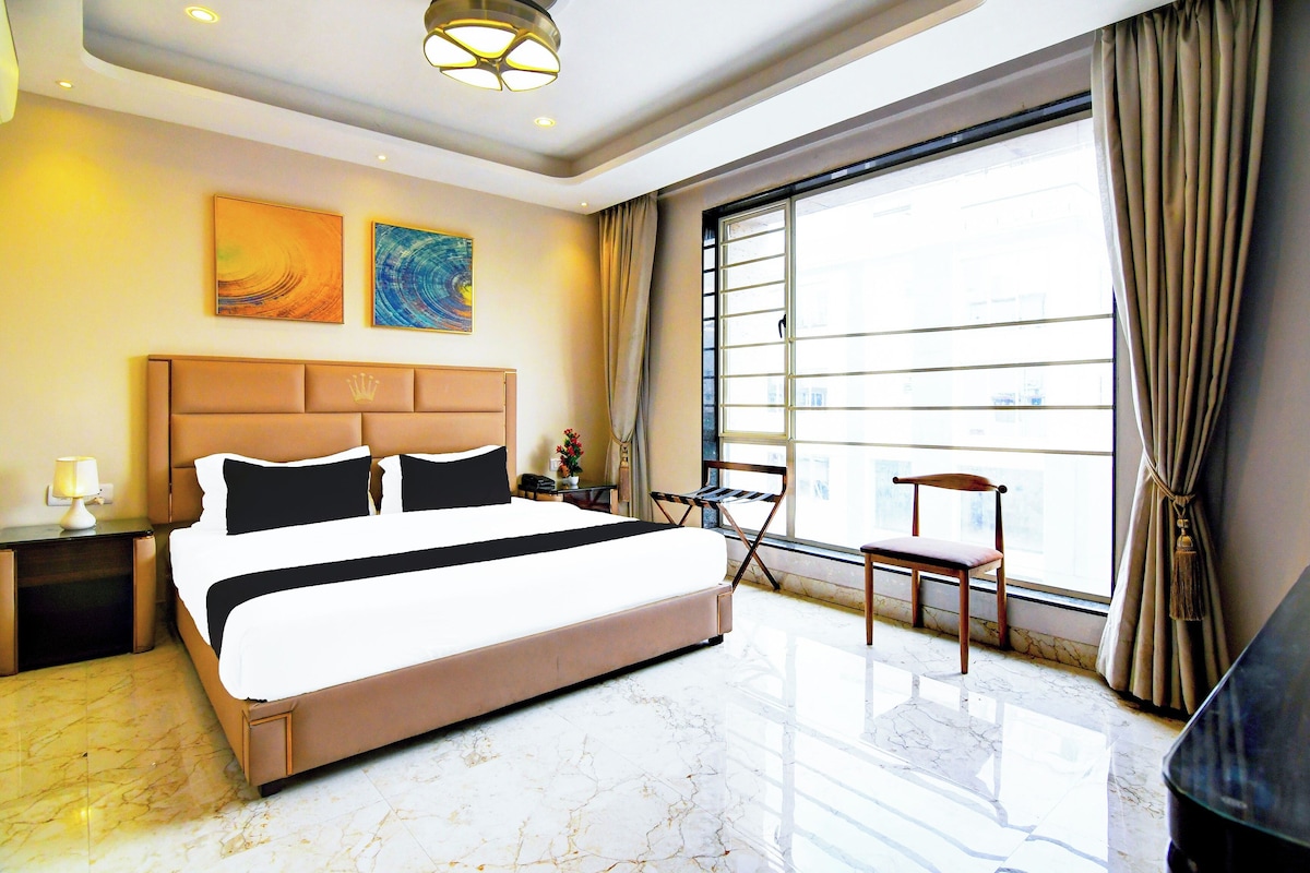 A hotel room with a large bed, a desk, a chair, a window with curtains, and artwork on the wall.