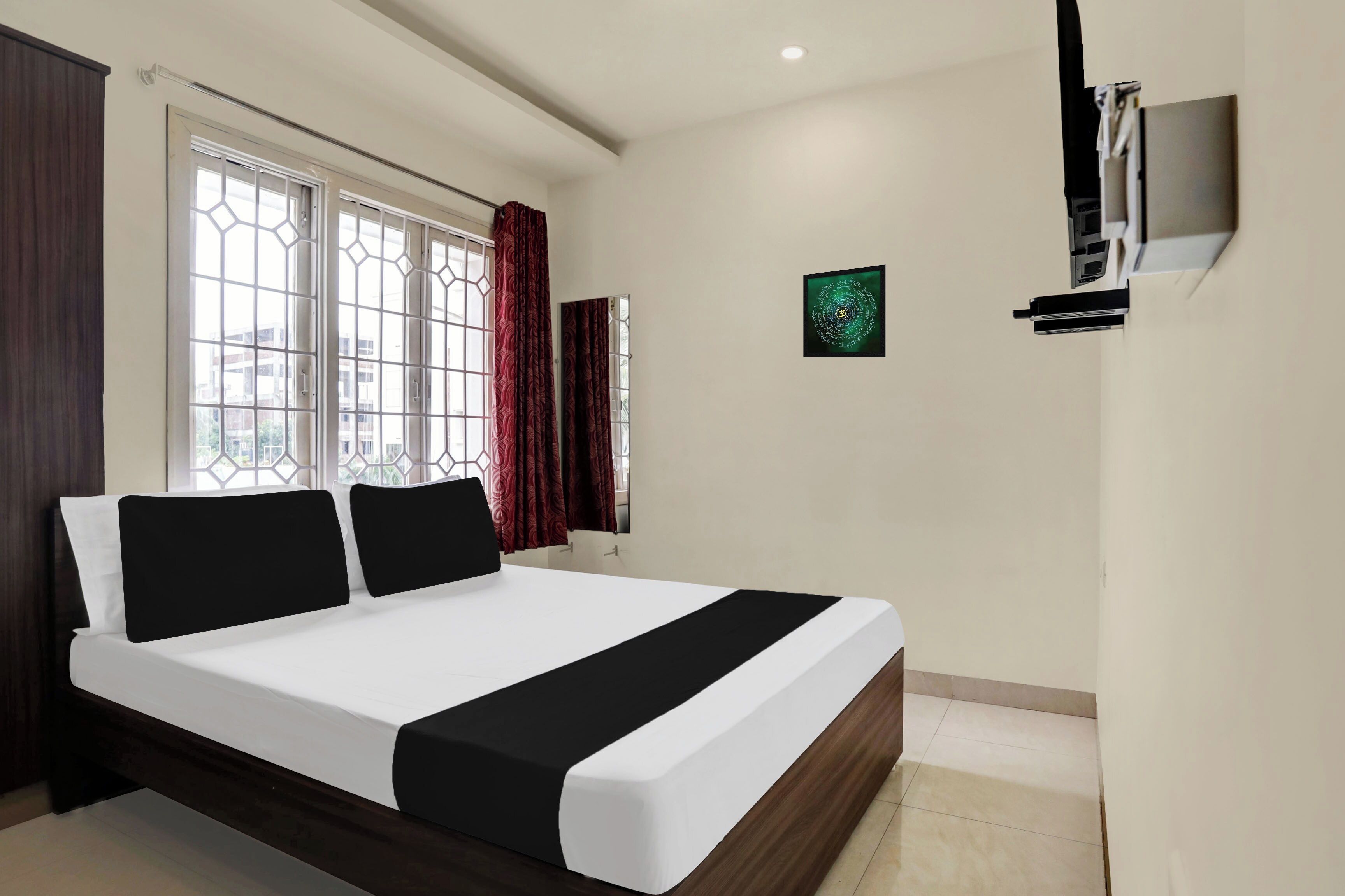 Habitación de hotel con cama, televisor montado en la pared y ventana con cortinas.