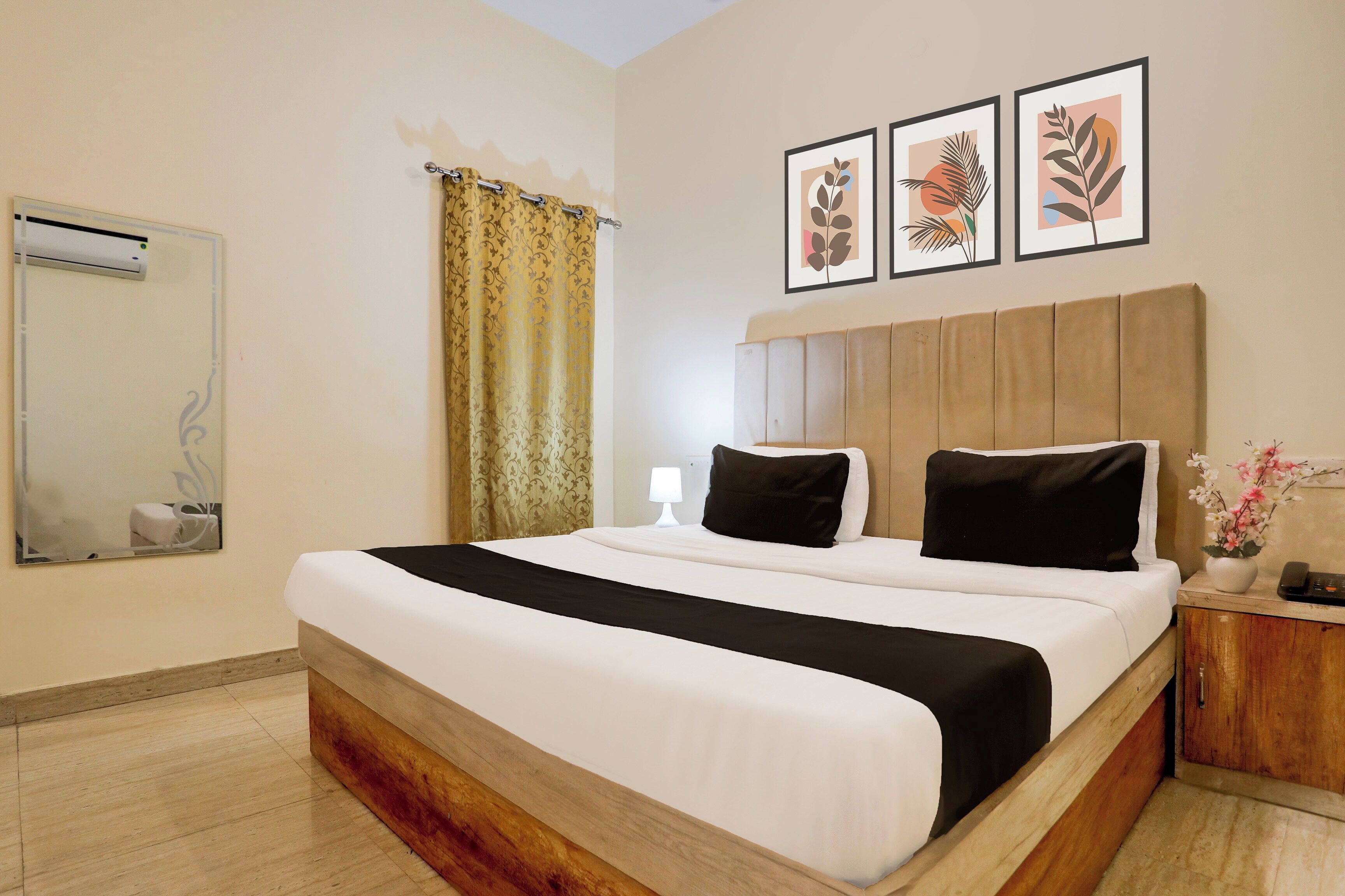 Una habitación de hotel con una cama grande, una mesita de noche con lámpara, un espejo y tres cuadros en la pared.