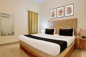 Ein Hotelzimmer mit einem großen Bett, einem Nachttisch mit Lampe, einem Spiegel und drei gerahmten Bildern an der Wand.
