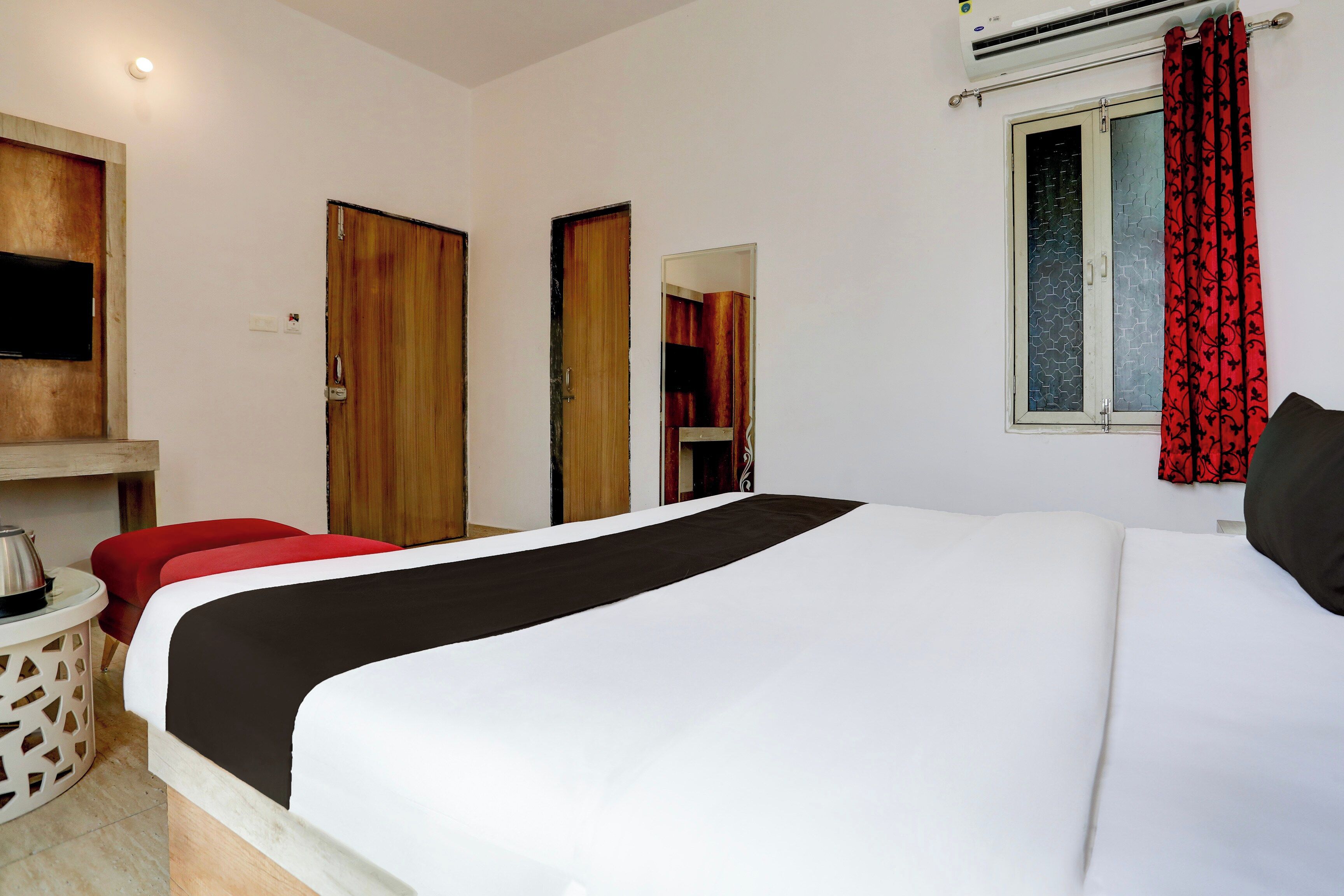 Una habitación de hotel con cama, televisor montado en la pared, ventana con cortinas y una puerta.