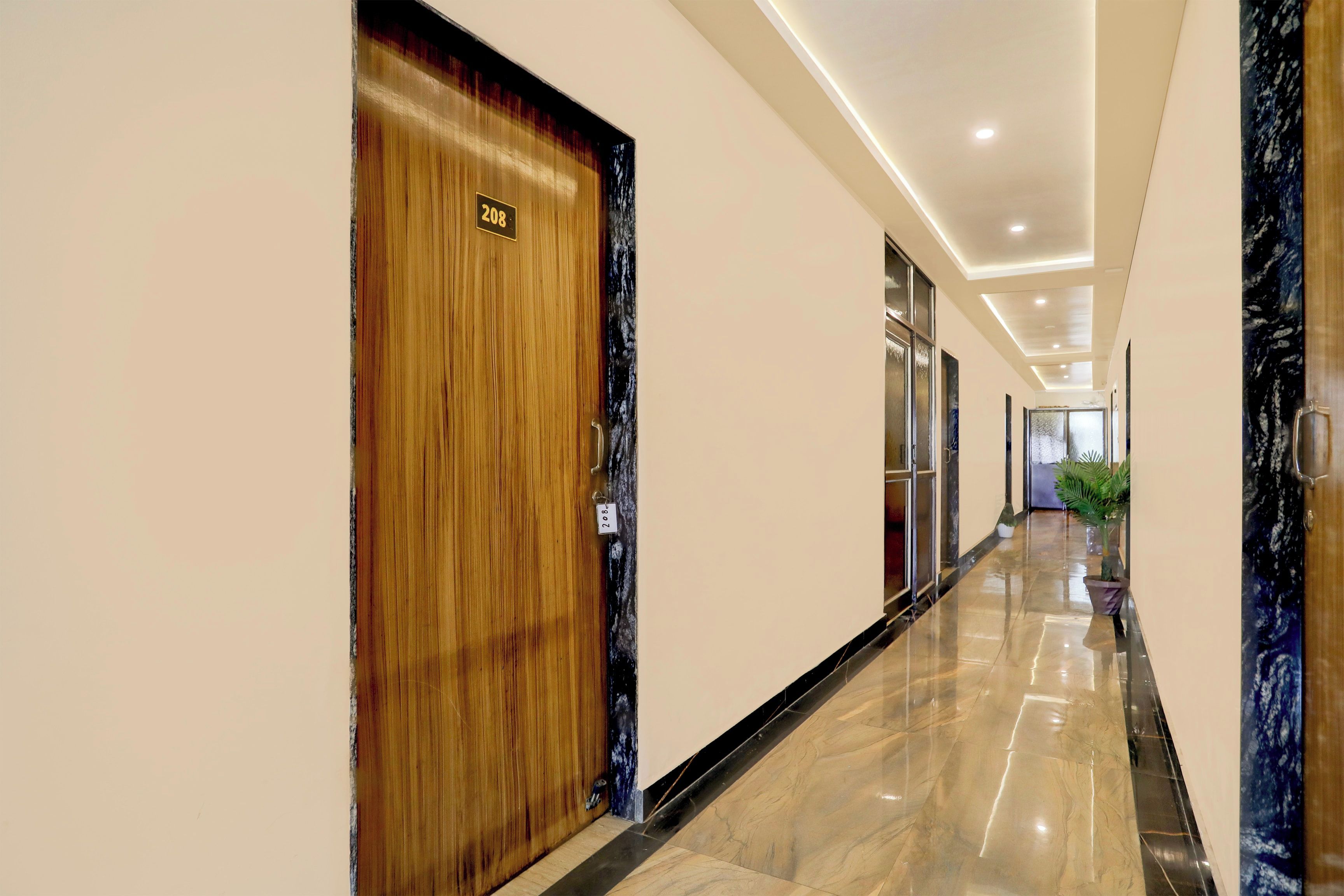 A hotel corridor with a wooden door labeled '208', a marble floor, and a plant in the distance.