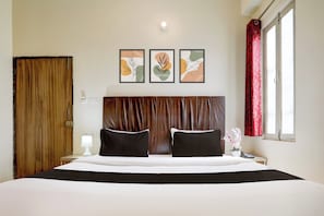 Ein Hotelzimmer mit einem großen Bett, zwei schwarzen Kissen, einem Holz-Kopfteil, einem Nachttisch mit einer Lampe und drei gerahmten Kunstwerken an der Wand.