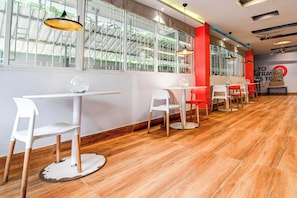 Interior de restaurante con suelo de madera, mesas y sillas blancas, y ventanas amplias con barrotes de metal.