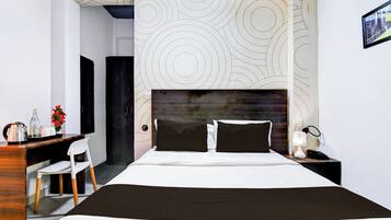 Une chambre d’hôtel comprenant un lit, un bureau avec une chaise, une table de chevet avec une lampe et un mur orné d’un motif circulaire.