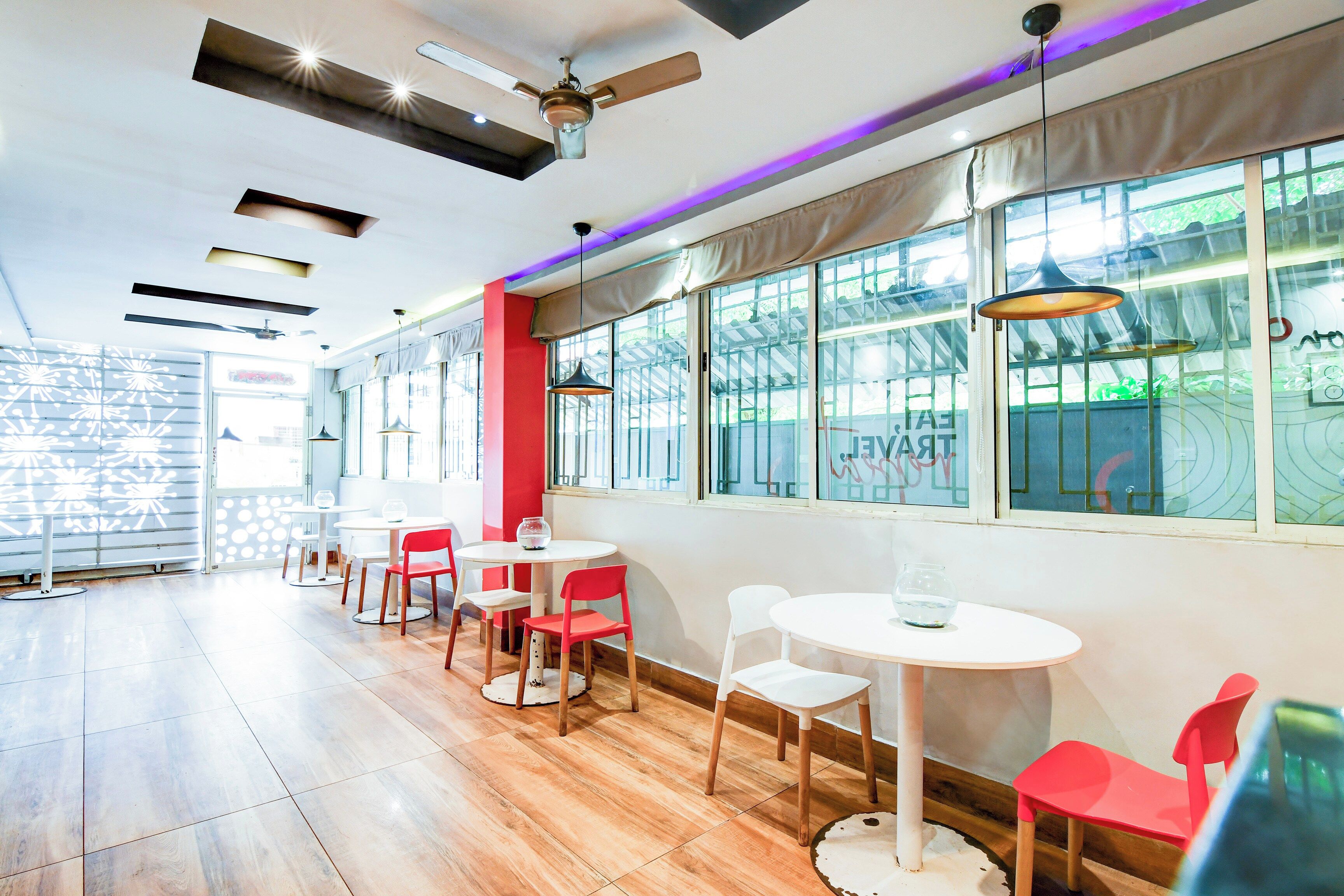Un restaurante con varias mesas y sillas, ventanas amplias y ventiladores de techo.
